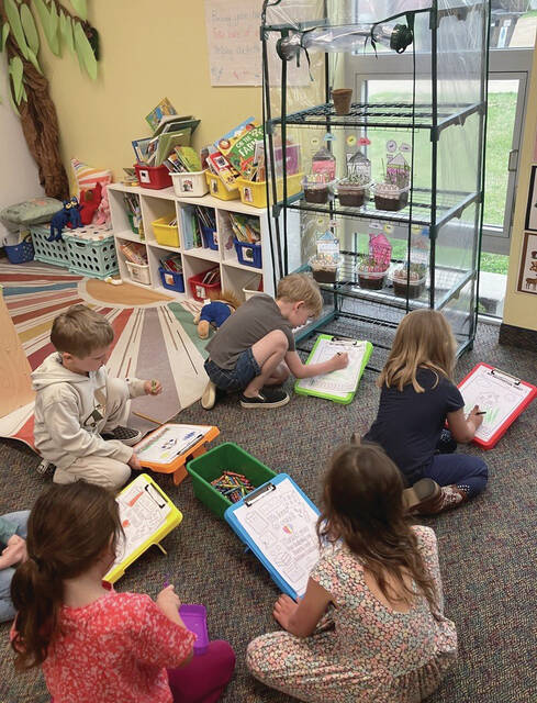 The preschoolers are observing how their grass is growing and filling out their observation sheet to show what they see.