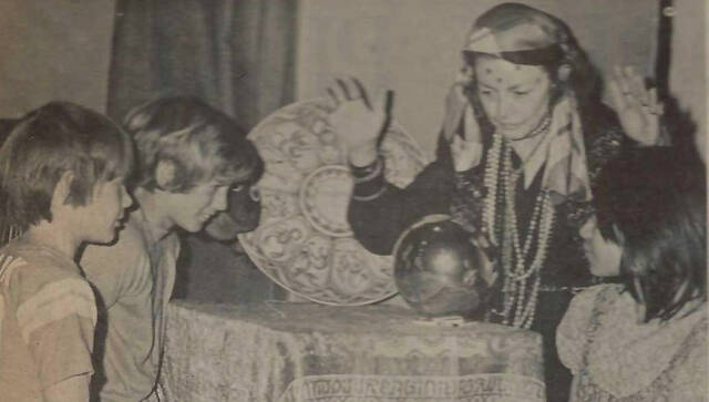 Plainsman file photo from May 19, 1974 Gypsy fortune teller and assistant librarian Alyce Bates presented the summer reading theme Your Future is in the Books to elementary students. Wilson School students Brian Pietz, Mark Niehus, and Gilda Fadgen are pictured here with Mrs. Bates.